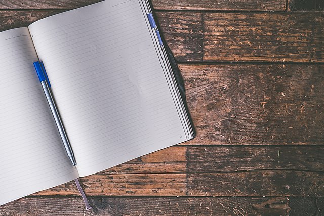 A blank journal, perfect for writing a Dungeons and Dragons session report, lying on a plank wood table.