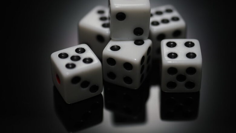 A photo of 6 white six-sided dice with black pips. One die is stacked atop the others. Dice like this can be used in TTRPG oracles like Motif Oracle Notebook.