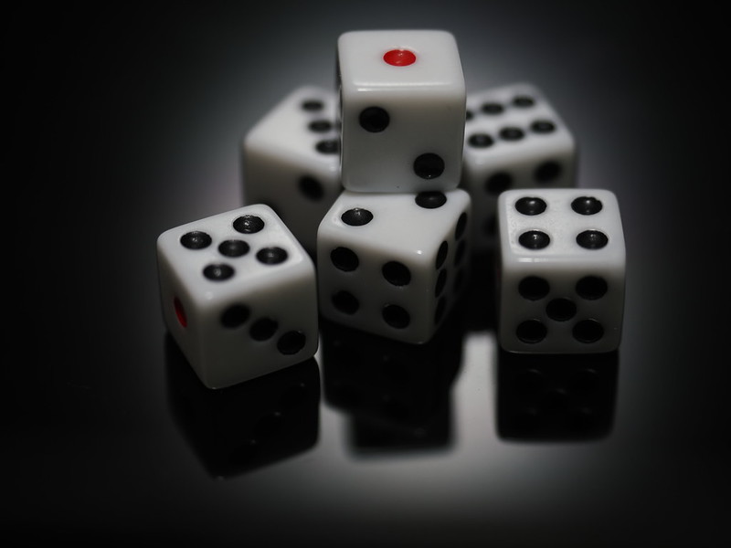 A photo of 6 white six-sided dice with black pips. One die is stacked atop the others. Dice like this can be used in TTRPG oracles like Motif Oracle Notebook.